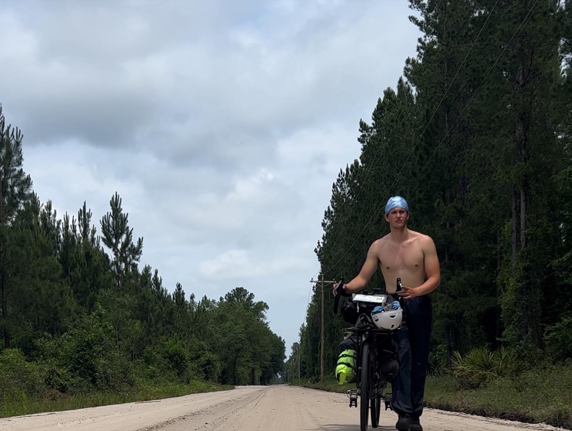 Pat pushing his fully loaded touring bike up an empty dirt road on the ride to Florida